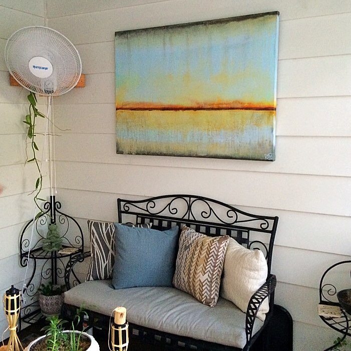 A cozy corner featuring a decorative iron bench with cushions, a plant stand, and a piece of abstract art hanging on the wall, complemented by a ceiling fan.