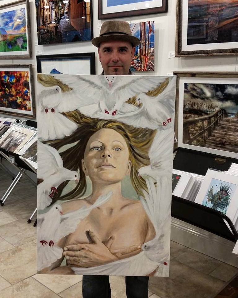 An artist holding a painting of a woman surrounded by white doves in an art gallery.