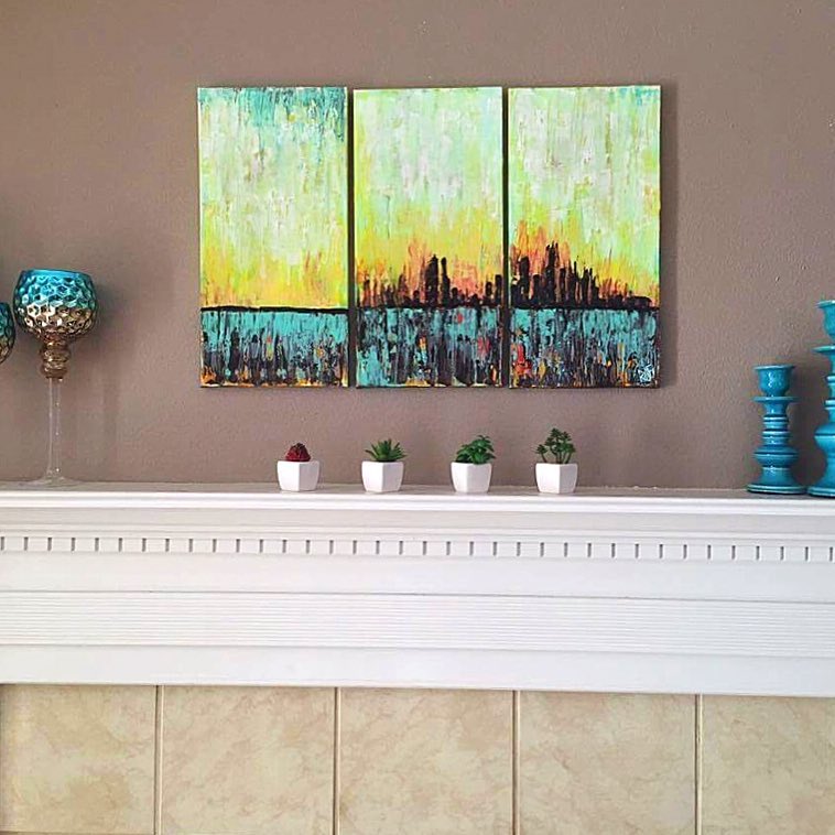 A vibrant three-panel abstract painting featuring shades of yellow, teal, and blue, displayed on a light-colored wall above a white mantel with small potted succulents and decorative teal accents.