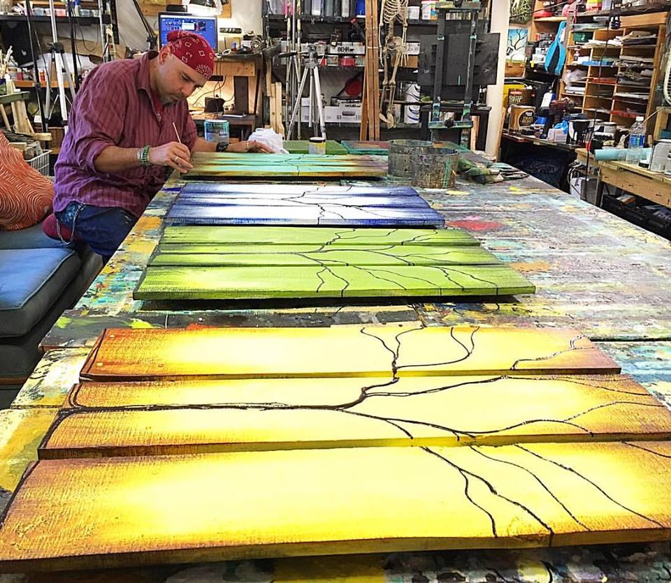 Artist working on colorful wooden panels in a creative studio, surrounded by art supplies and tools.