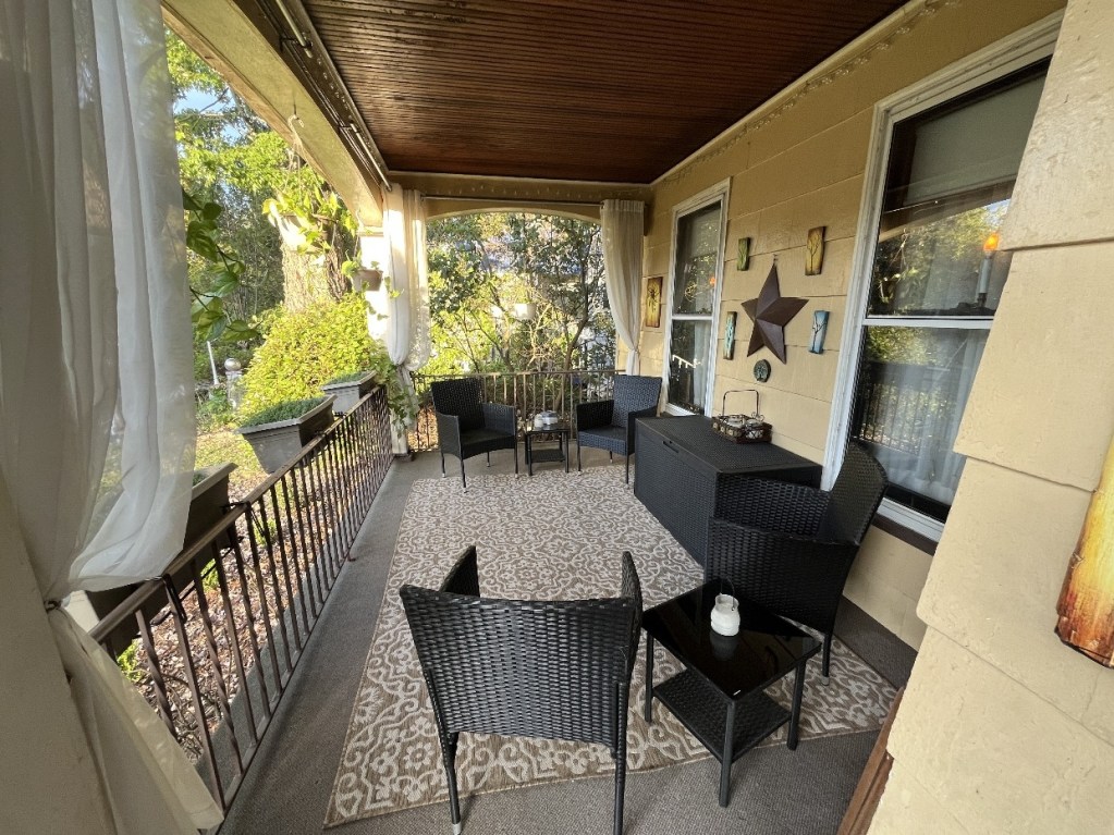 A cozy porch area with four black wicker chairs and a small table, adorned with decorative elements and surrounded by greenery.