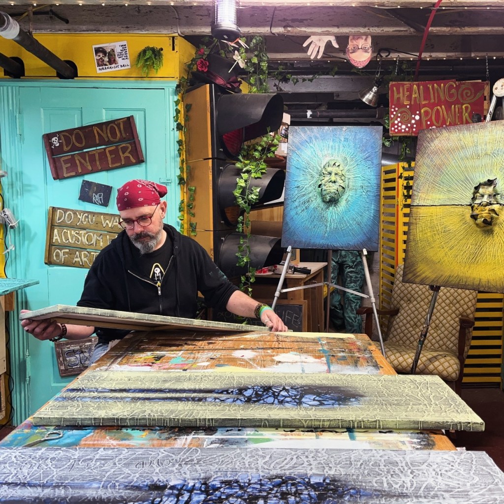 An artist in a studio, examining a canvas with intricate textures, surrounded by vibrant artwork and creative decor.