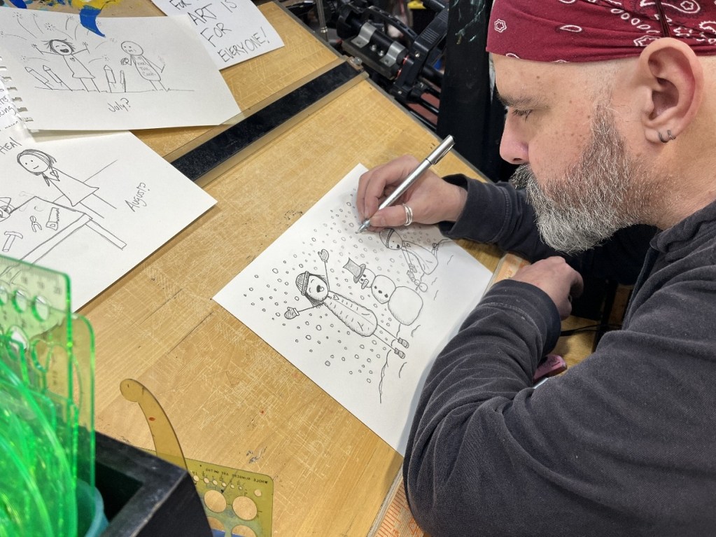 An artist sketching a whimsical snowman illustration in a studio filled with drawing supplies and sketches.