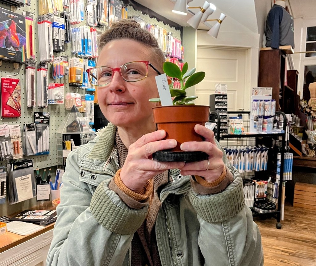 A person holding a small potted jade plant in a store filled with art supplies and tools.