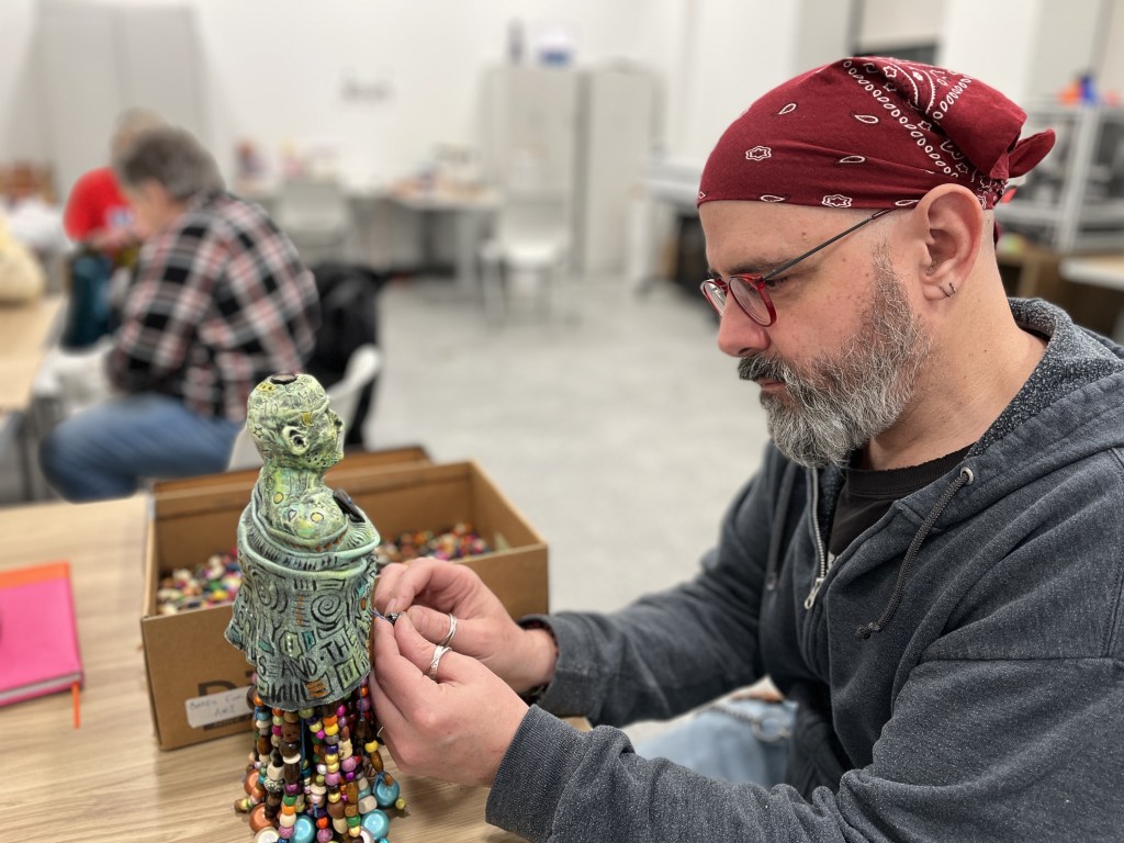 An artist working on a colorful sculpture in a studio setting, surrounded by craft supplies and other people engaging in creative activities.