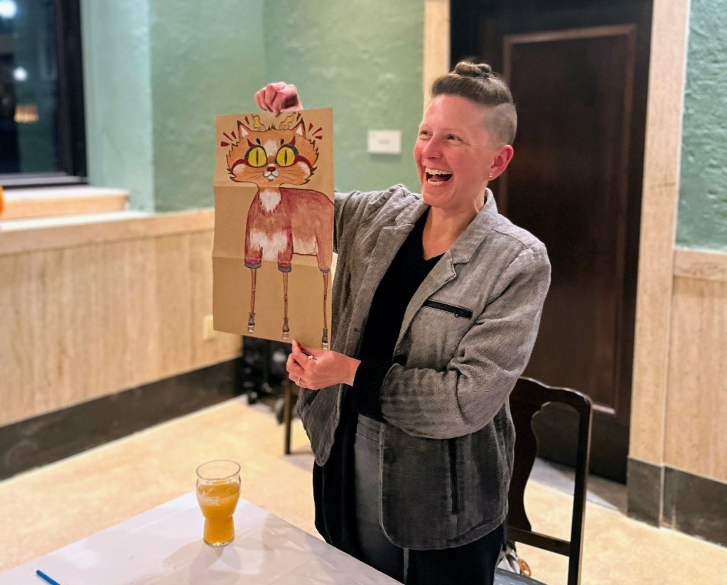 A person joyfully holding up a colorful artwork featuring a cartoon-like character, surrounded by a festive atmosphere.