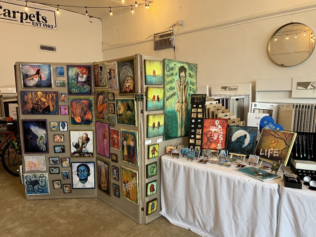 Display of various pieces of artwork, including paintings and magnets, set up at an art event.