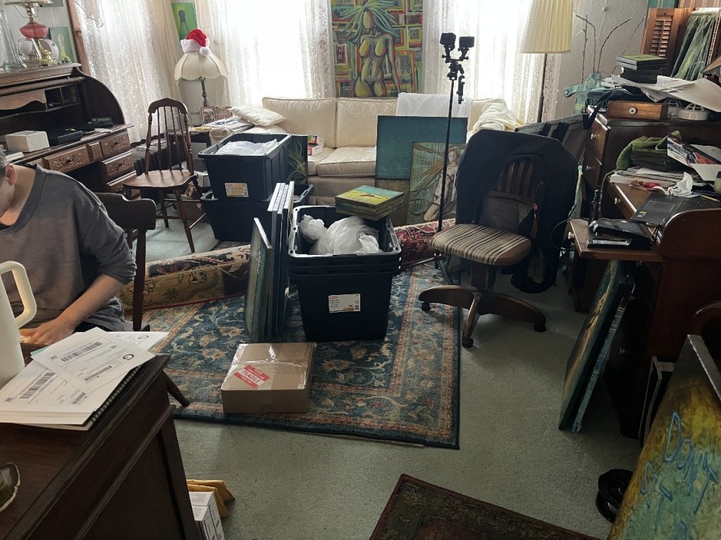 A cluttered studio space filled with art supplies, boxes, and unfinished artwork, showcasing a creative environment in disarray.