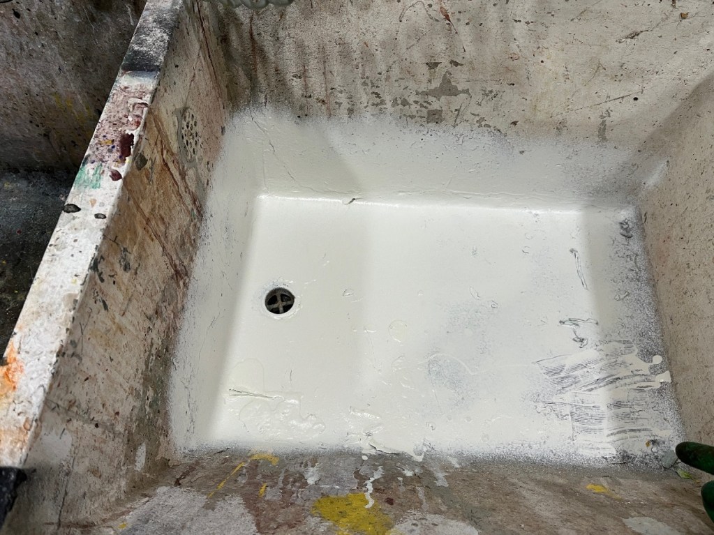 A close-up view of a utility sink with fresh white flex seal coating applied, showing uneven patches and a drain at the bottom.