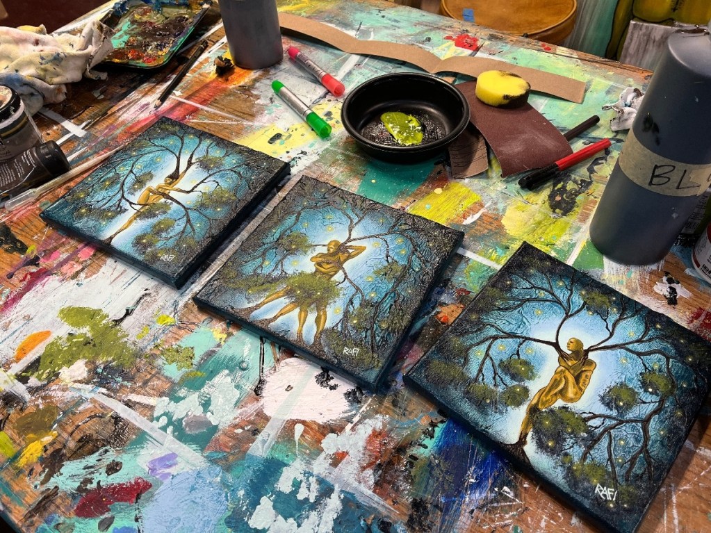 Three miniature paintings titled 'Nature of Being' displayed on an artist's workspace, surrounded by paint supplies and colorful paints.