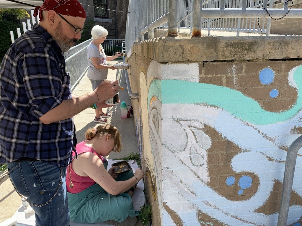 Artists painting a mural at the Oil City Library, featuring colorful waves and a vibrant design on the wall.