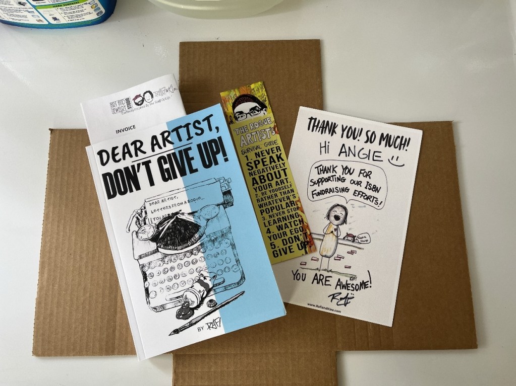A flat lay image featuring the book cover of 'Dear Artist, Don't Give Up!' alongside a thank you card and an invoice on a brown cardboard surface.