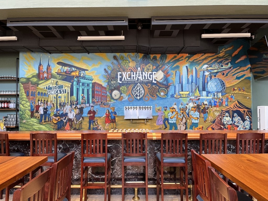 A colorful mural at The Exchange in Oil City, featuring scenes of local history, community gatherings, and cultural elements, with the text 'EXCHANGE' prominently displayed.