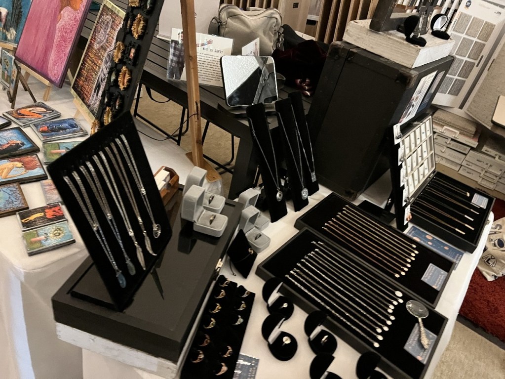 Display of handmade jewelry and art pieces at a pop-up shop, showcasing various necklaces, rings, and artwork.