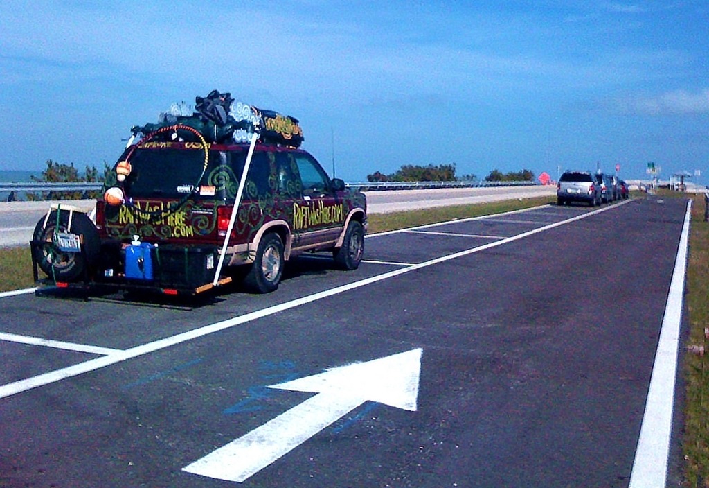 A colorful vehicle parked on the side of a road, decorated with various items and a website URL visible on the back.