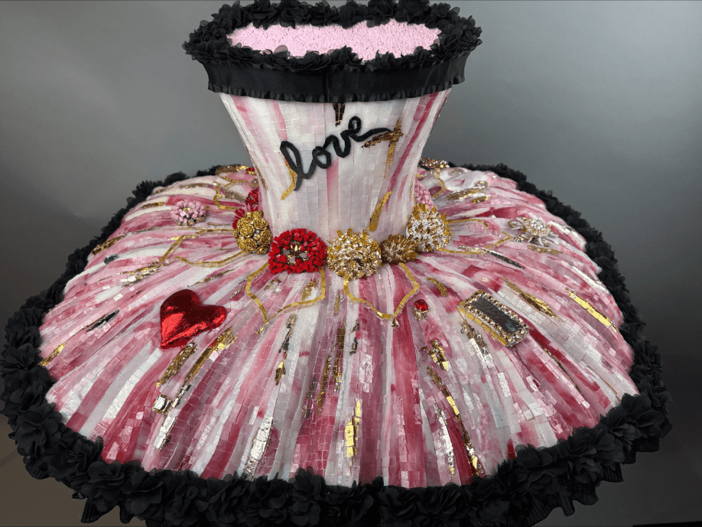 A decorative dress form covered in pink and white strips, embellished with gold accents, flowers, and hearts, featuring the word 'love' embroidered on the bodice.