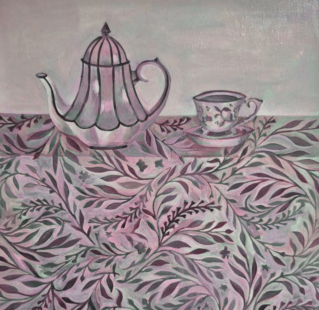 A teapot and teacup are arranged on a decorative tablecloth featuring intricate leaf patterns in shades of pink and green.