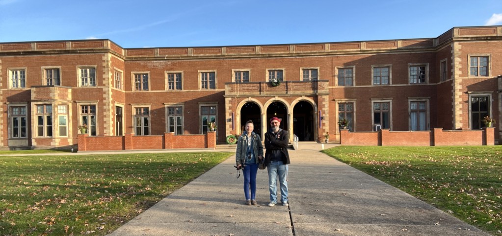 A man and a woman standing on a pathway in front of a large brick building with multiple windows and a green lawn.