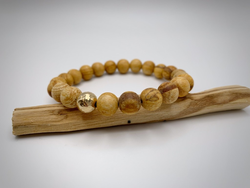 A natural wood bead bracelet with a golden accent bead, displayed on a piece of driftwood.
