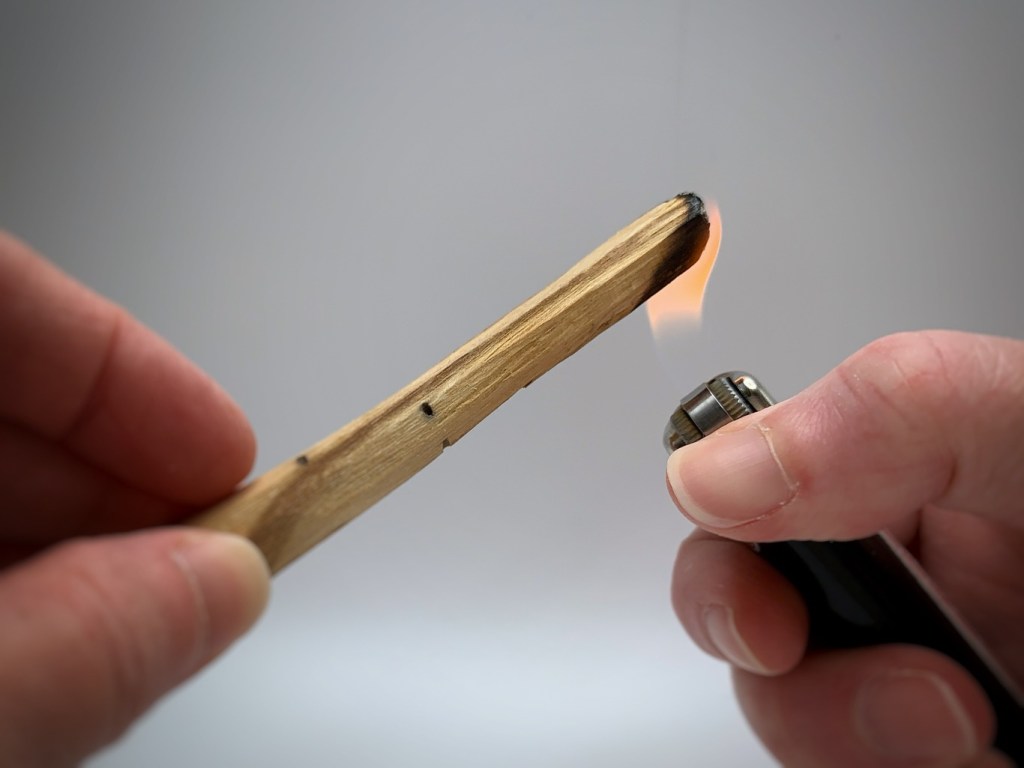 A hand holds a wooden stick as a lighter ignites its end, producing a small flame.