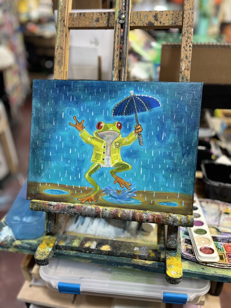 A colorful painting of a frog wearing a yellow raincoat and holding a blue umbrella, standing in the rain on a wooden platform with puddles.